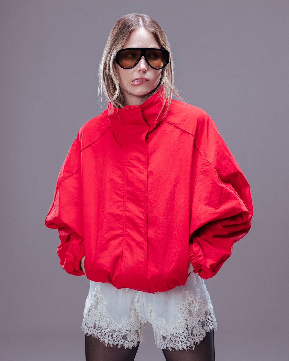 THE FIT: half-body portrait in a high-neck red jacket and amber sunglasses