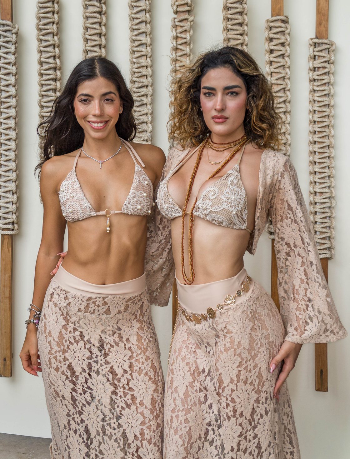 Two models in nude lace styling by Vulcano Swimwear against a rope wall